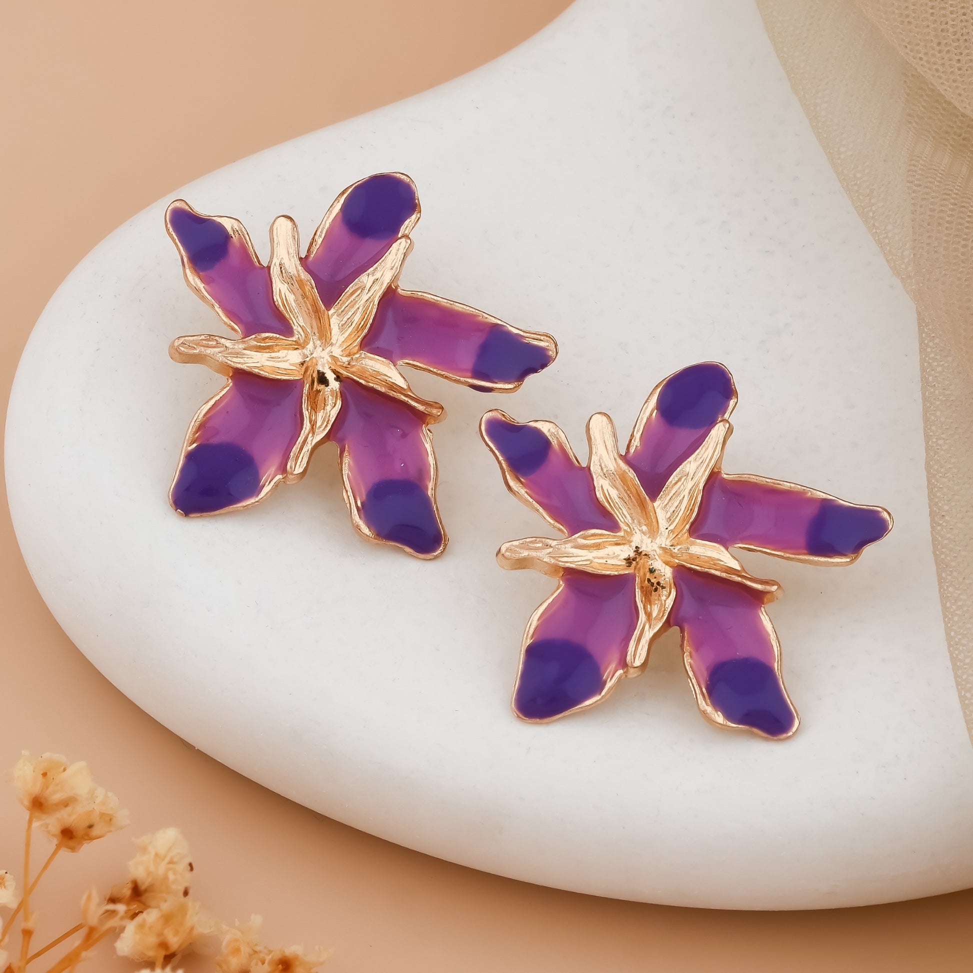 Purple and gold starfish-shaped earrings on a white stone with a beige background