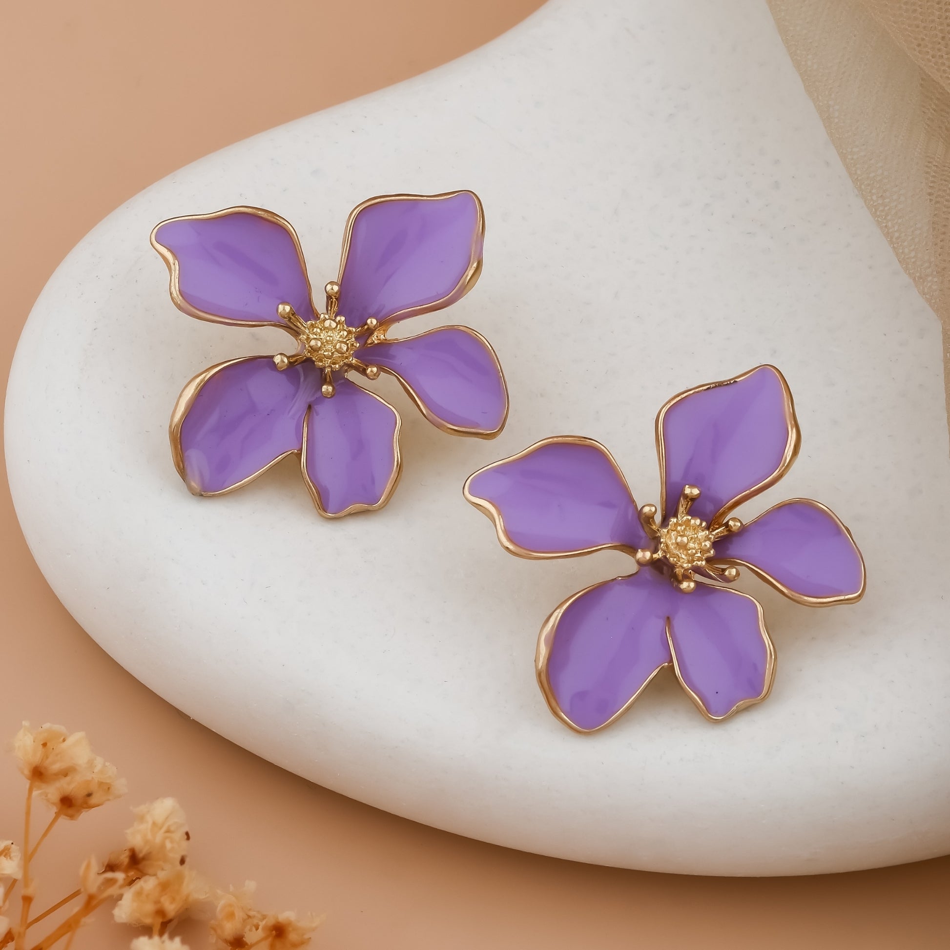 Purple flower-shaped earrings with gold accents on a white stone background